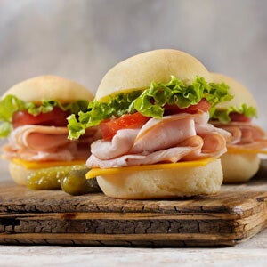 A wooden board with three hamburger sandwiches.