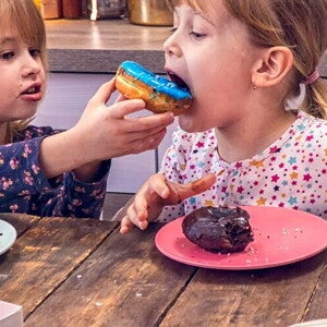 Two girls eating donuts together in the kitchen.