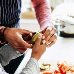 An adult helping a child to prepare fruit and vegatables