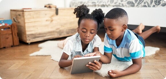 children lying on the floor playing on a tablet children lying on the floor playing on a tablet