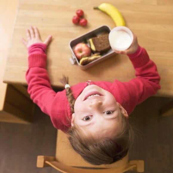 A girl sitting at a table eating her meal looking up.